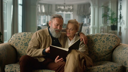 Smiling old couple looking photo album room. Mature man woman talking home.