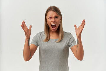 Indoor shot of mad, angry young female, starring into camera and raised her hands while screaming. Isolated over white background