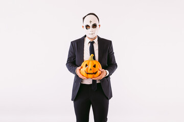 Man dressed in suit and tie, wearing a Halloween cross-browed killer mask, holding a pumpkin Jack-o-lantern. Carnival and halloween celebration
