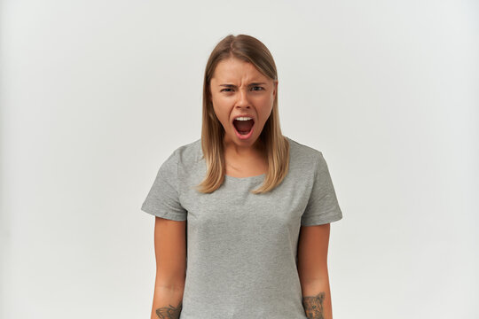 Indoor shot of mad, angry young female, starring into camera while screaming. Isolated over white background