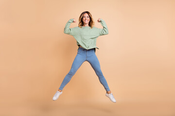 Full length body size view of lovely cheerful woman jumping showing stength isolated over beige pastel color background