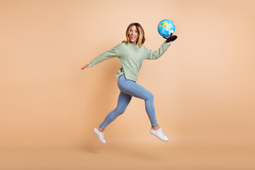 Full length body size photo woman jumping high running keeping globe isolated pastel beige color background