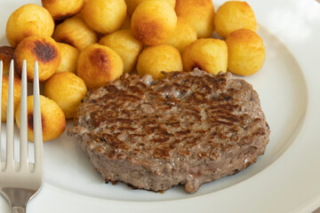 steak haché de boeuf et  pommes de terre dauphine cuites sur du papier sulfurisé