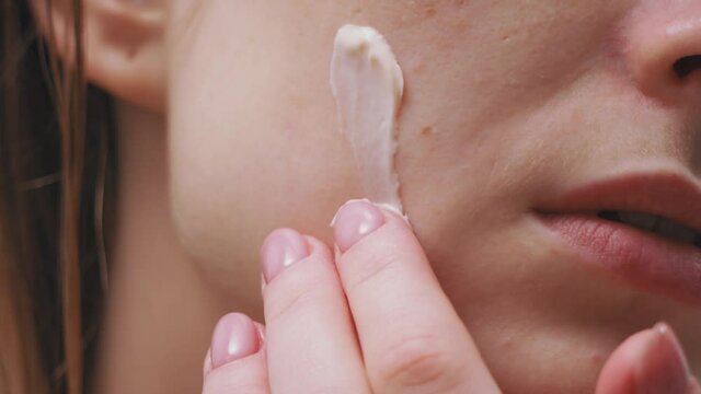 Beauty treatment. Female model applying nourishing cosmetic product on face. Attractive young caucasian woman massaging facial skin with creme. Closeup view.
