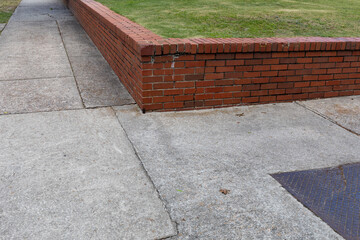 Low red brick retaining wall separating a grassy area from sidewalks, corner view at an...