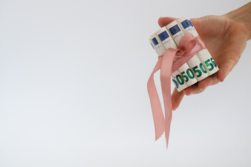 Female hand holding 50 euro bills in rolls, tied with pink gift ribbon.