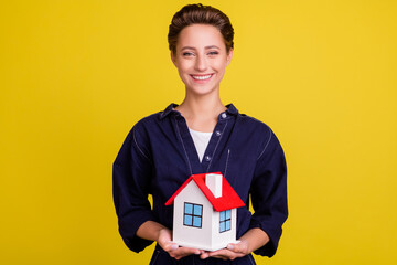 Fototapeta na wymiar Portrait of attractive cheerful girl holding in hands new cottage house flat figure isolated over bright yellow color background