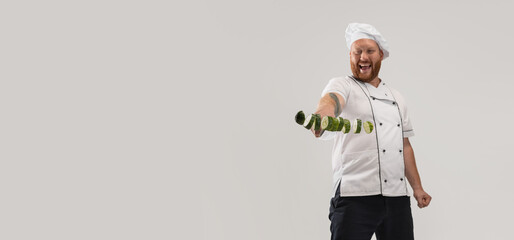 Unique cutting of vegetables. One hadsome bearded man, cook, male chef in white uniform cut cucumber isolated on white background.