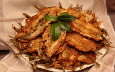 Crispy deep fried small fish on a plate, decorated with bay leaves and spices. Dough herring. Herring recipes