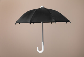 Open small black umbrella on beige background