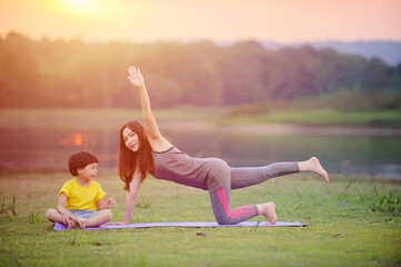 Mother and child doing yoga exercises at the nature park before sunset