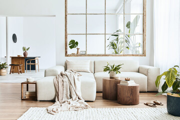 Fototapeta premium Modern interior of open space with design modular sofa, furniture, wooden coffee tables, plaid, pillows, tropical plants and elegant personal accessories in stylish home decor. Neutral living room.