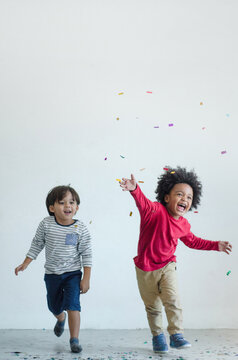 Two boys of different nationalities having fun chasing confetti on white background, friendship between different races and religions