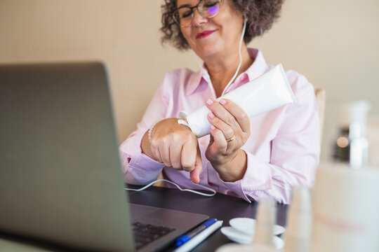 Crop businesswoman applying nourishing cream on hand during video chat