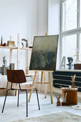 Unique artist workspace interior with stylish teak commode, wooden easel, bookcase, artworks, painting accessories, decoration and elegant personal stuff. Modern work room for artist. Template.