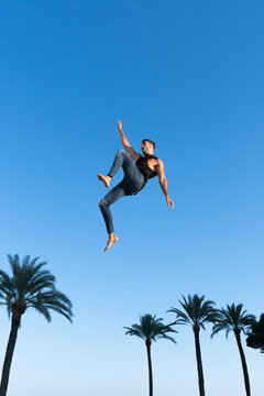 Active dancer jumping against palm tree under blue sky