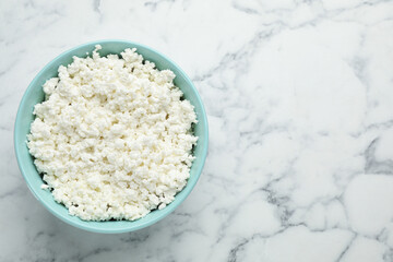 Delicious fresh cottage cheese in bowl on white marble table, top view. Space for text