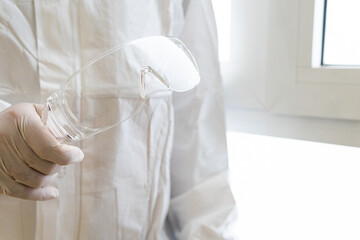 Anonymous doctor in PPE suit putting on glasses in clinic