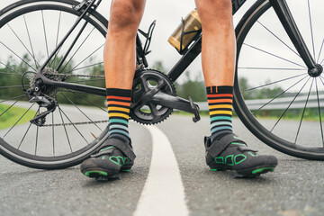 Crop bicyclist in cycling shoes with bike on road