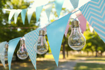 Colorful bunting flags with light bulbs in park. Party decor