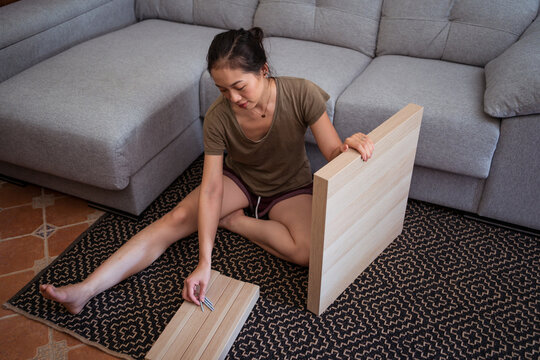 Asian woman assembling table on rug at home