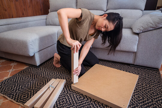Ethnic woman assembling table on rug at home