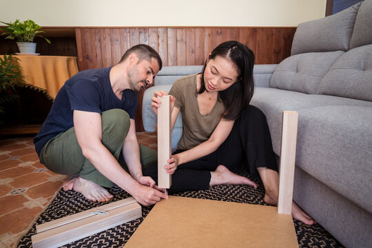 Multiracial couple assembling table on rug in house