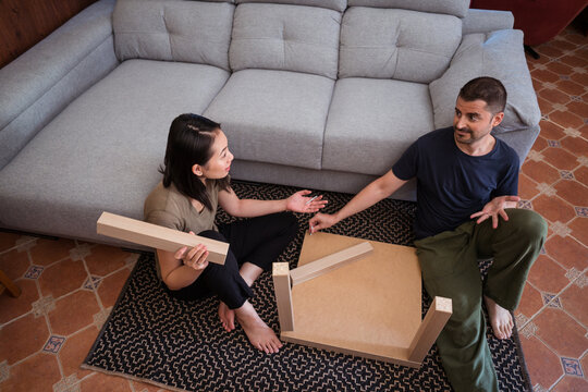 Multiracial couple assembling table on rug in house