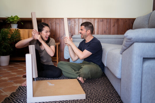 Happy multiethnic couple having fun with table legs at home