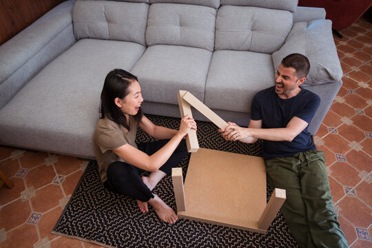 Multiracial couple assembling table on rug in house