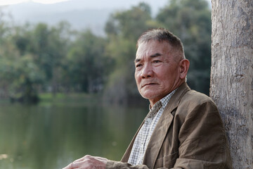 Asian old man sitting and he worry about his family financial in public park