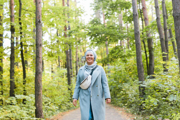Naklejka na ściany i meble Islamic young woman wearing hijab standing on autumn park background. Modern arabian muslim girl.