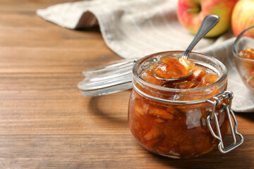 Tasty apple jam and spoon in glass jar on wooden table, closeup. Space for text
