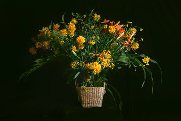 A fancy bouquet of yellow wildflowers with lilies on a dark background. Still-life. In the style of...