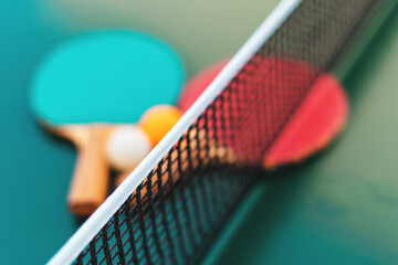 Table tennis rackets and ping-pong balls on green table surface with net