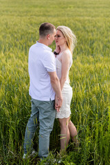 A young couple holding hands and walking through wheat field. Vertically framed shot.