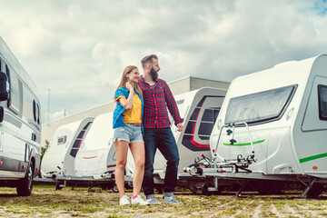 Woman and man choosing camper van to rent or buy on yard of dealer