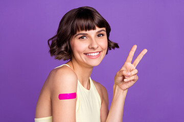 Photo of cheerful happy young woman vaccine patch make v-sign good isolated on violet color...