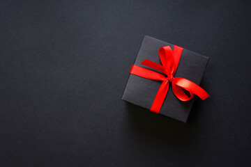 Black Friday elegant background with a black gift box and red bow ribbon. Top view. Composition with copy space.