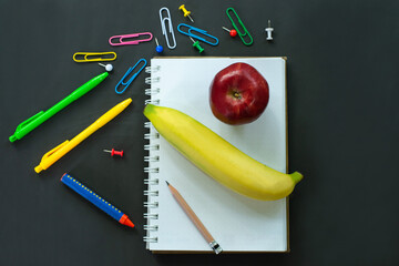 School supplies and office supplies on blackboard with bananas and apples on notebooks of Back to School ideas. Smooth top view with copy space for your text.