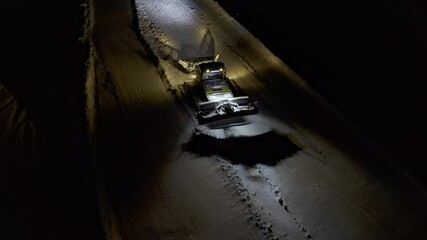 Snow grooming machine on a ski slope at night. View from above