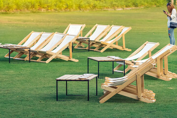 Many empty white deck chairs with tables for dinner in lawn is surrounded by shady green grass. Comfortable on outdoor patio chairs in garden.Lawn chairs in park.Sunbeds in the garden.Selective focus.