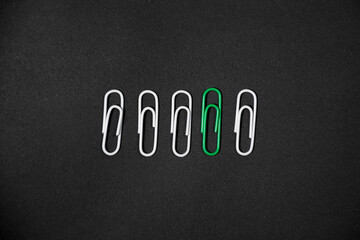 Green paper clip in the middle of white clips row. unique idea concept. Isolated on Black Background