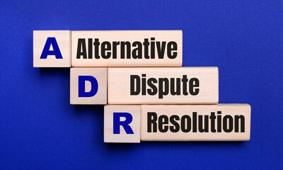 On a bright blue background, light wooden blocks and cubes with the text ADR Alternative Dispute...