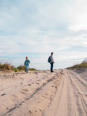 Happy father and daughter running jumping having fun on empty autumn sea beach. Dad and child walking on white sand road with reeds blue sky background. Lifestyle real people. Happiness travel concept