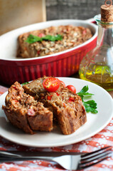 Homemade eggplant casserole with bell peppers, onions, garlic, parsley on a wooden board on a gray background. Stewpan with eggplant casserole and slice of eggplant casserole on white plate