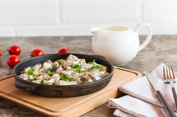 stewed mushrooms in sour cream and parsley in a frying pan on a wooden stand.