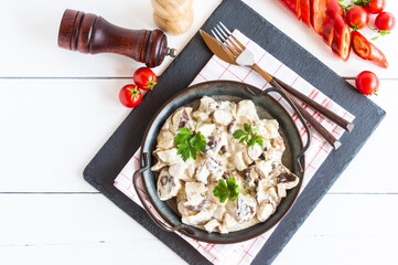 creamy mushroom sauce with pieces of white mushrooms with spices in a frying pan. top view. white wooden background.