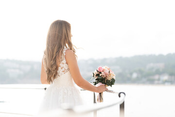 Brunette bride in white dress looking at the sea 