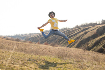 A young man jumping yellow t-shirt and white sneakers in spring mountains at sunset and enjoying view of nature. Mountain and coastal travel, freedom and active lifestyle